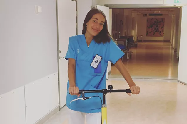 Läkarstudenten Isabella står i läkarrock på en sparkcykel nere i kulverterna på sjukhuset.