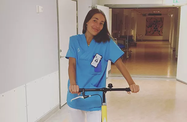 Läkarstudenten Isabella står i läkarrock på en sparkcykel nere i kulverterna på sjukhuset.